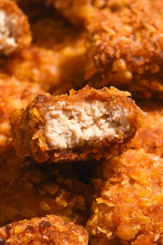 A macro close up image of gluten free tofu nuggets. The central nugget has been bitten into, revealing the juicy 'meat' centre and golden brown crumb