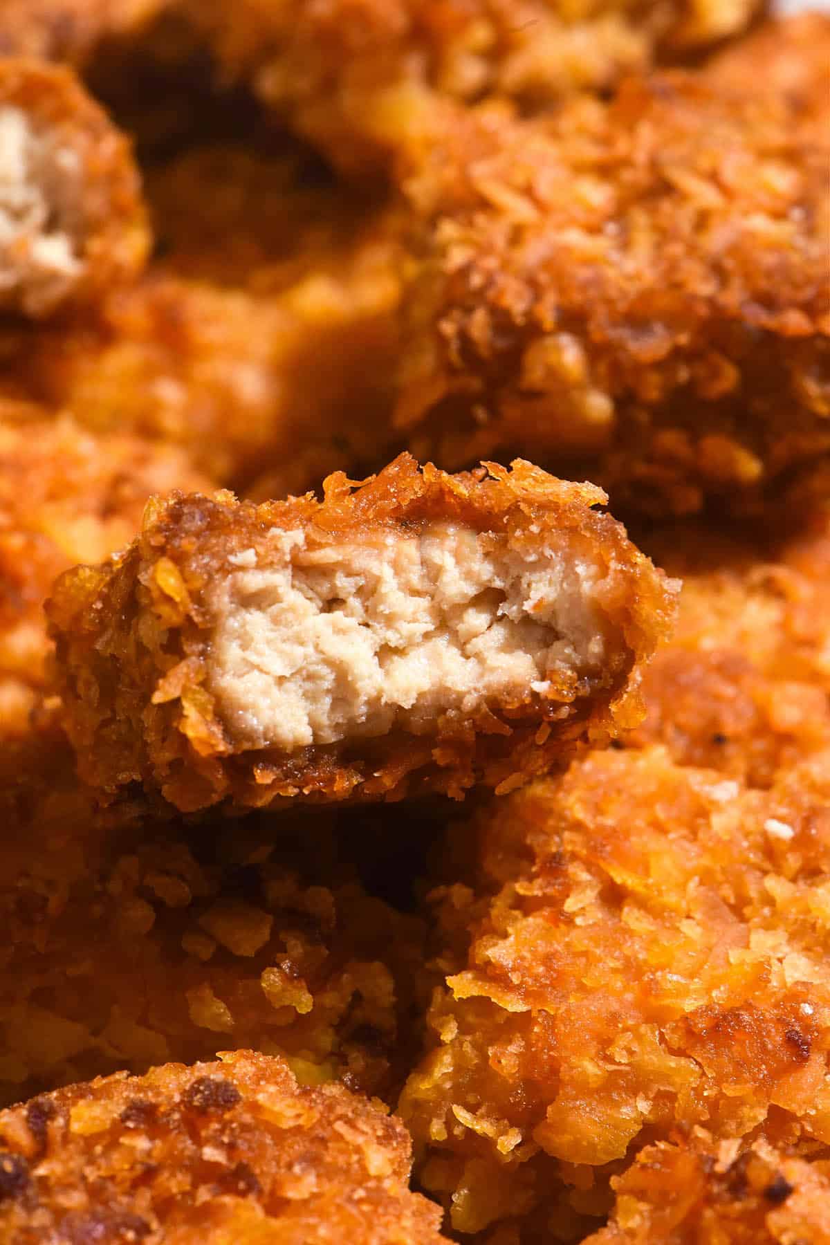 A macro close up image of gluten free tofu nuggets. The central nugget has been bitten into, revealing the juicy 'meat' centre and golden brown crumb