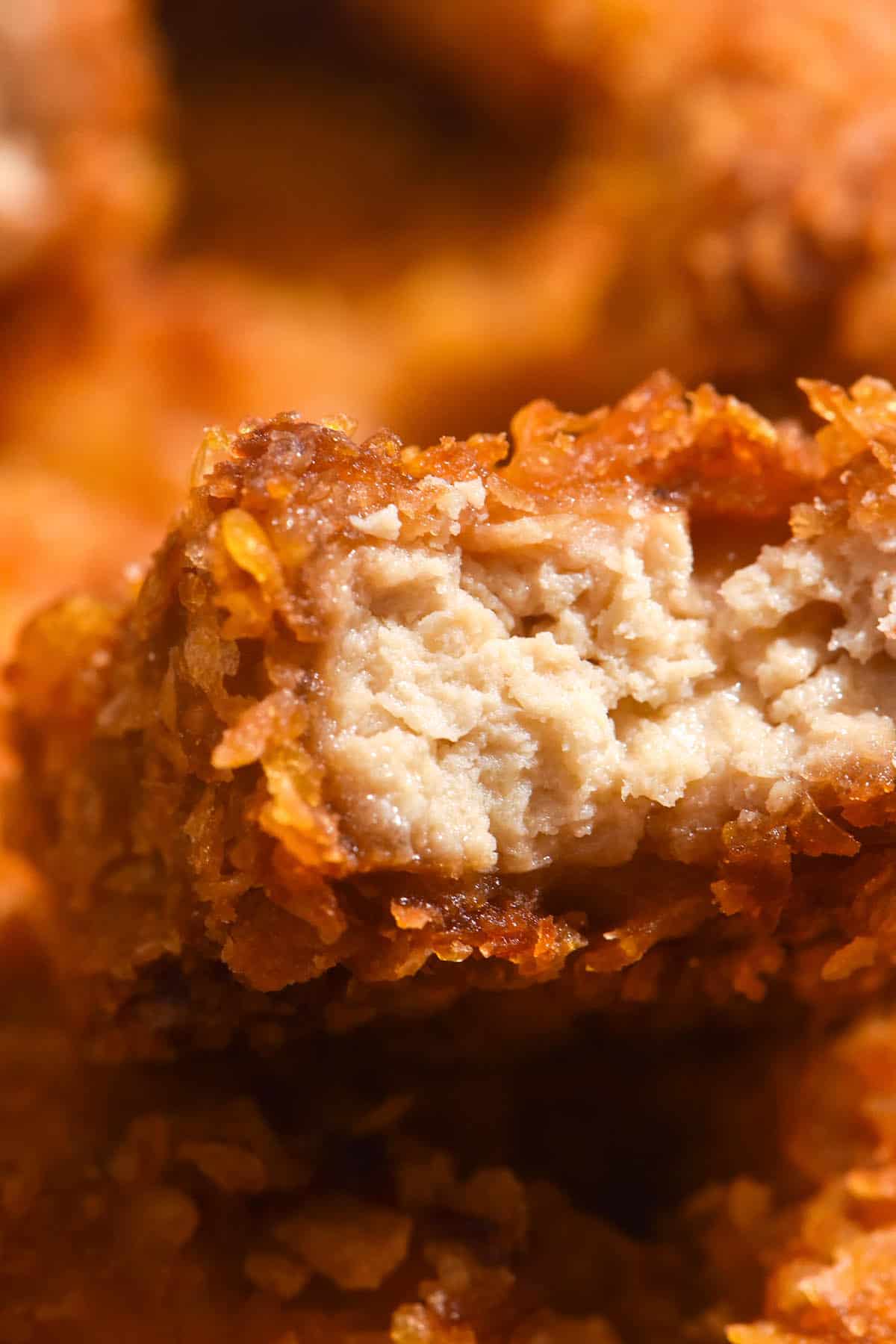 A macro close up of a gluten free tofu nugget that has been bitten into, revealing the juicy inside and the golden brown crumb