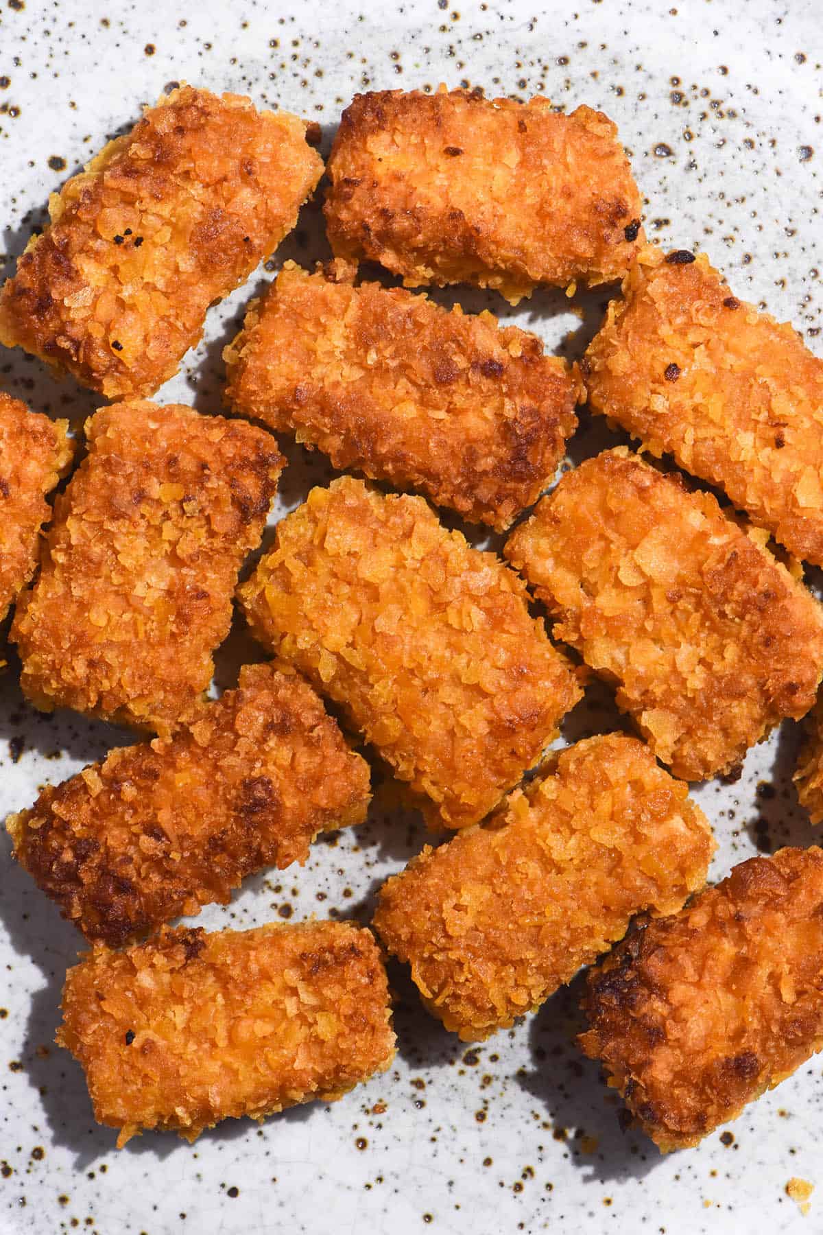 A brightly lit aerial image of gluten free tofu nuggets on a white speckled ceramic plate