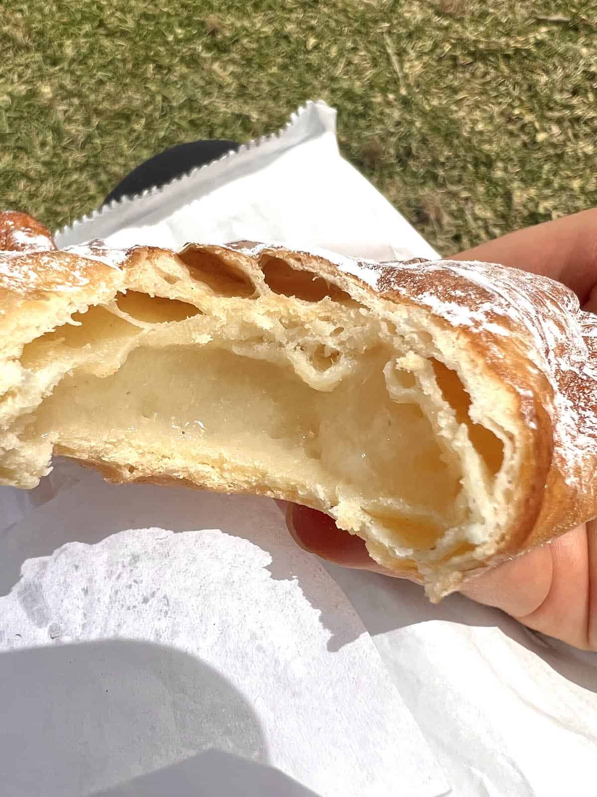 A cream filled gluten free pastry that has been bitten into, revealing the crumb and the cream filling inside. 