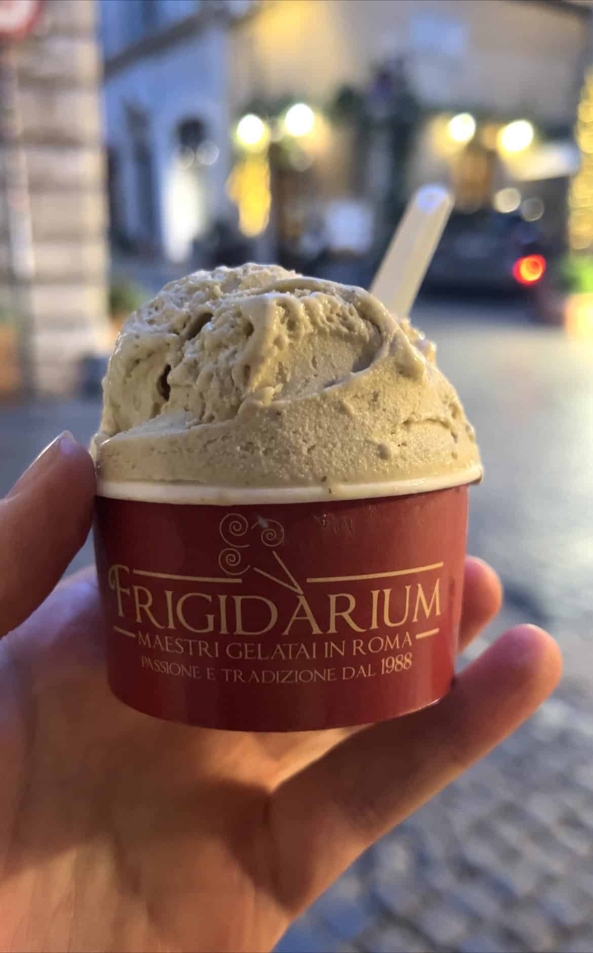 A night time image of a cup of gelato from Frigidarium in Rome. A person holds the cup of gelato against the backdrop of a cobbled Roman street.