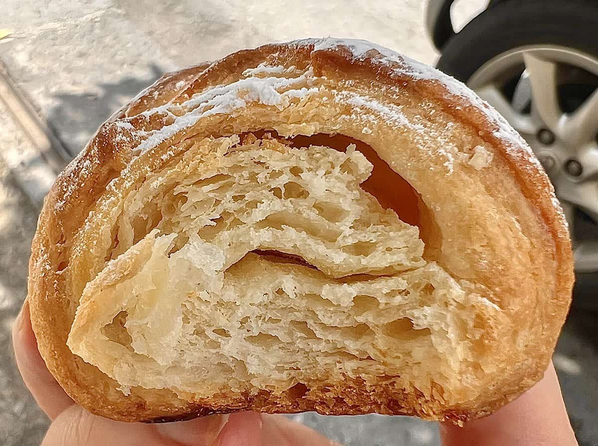 An image of a gluten free croissant from Artigiani Del Senza Glutine in Catania, Sicily. The croissant has been bitten into, revealing the flaky layers inside.