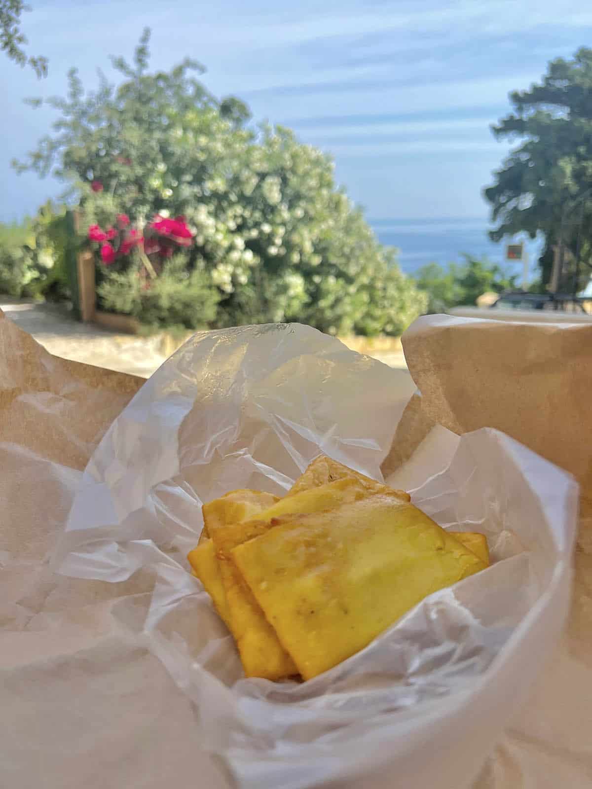 An image of fresh panelle (fried chickpea fritters) with a view of Scopello, Sicily in the background