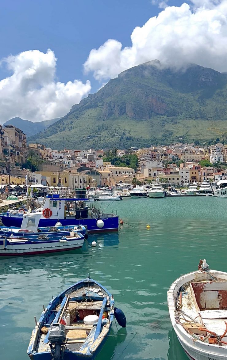 An image of the houses of Castellamare Del Golfo as seen from the port with boats and aquamarine waters in the foreground
