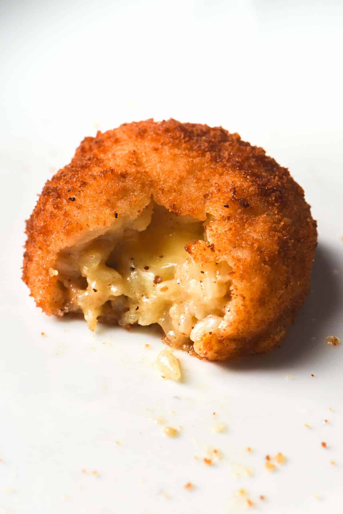 A close up image of a gluten free arancini on a white place. The arancini has been torn, revealing the molten mozzarella inside. 