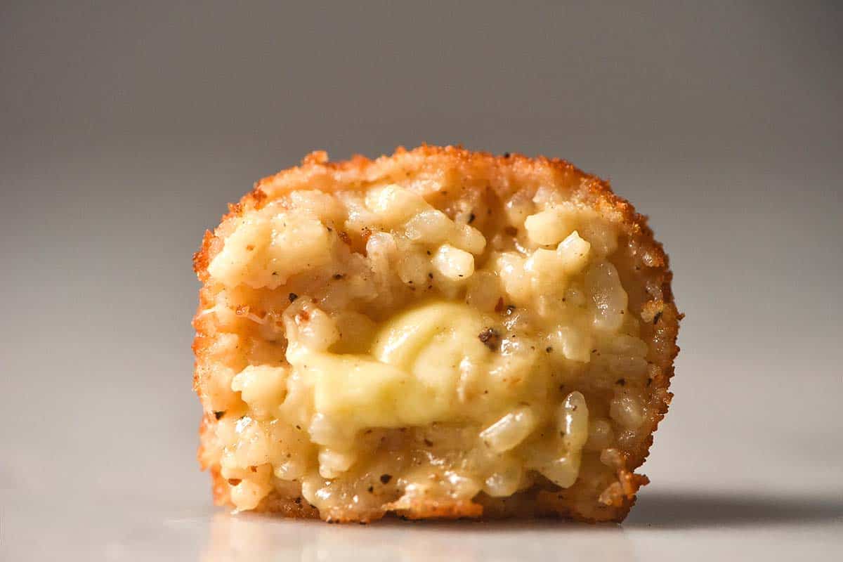 A side on macro image of half a gluten free arancino on a white marble table against a white backdrop.