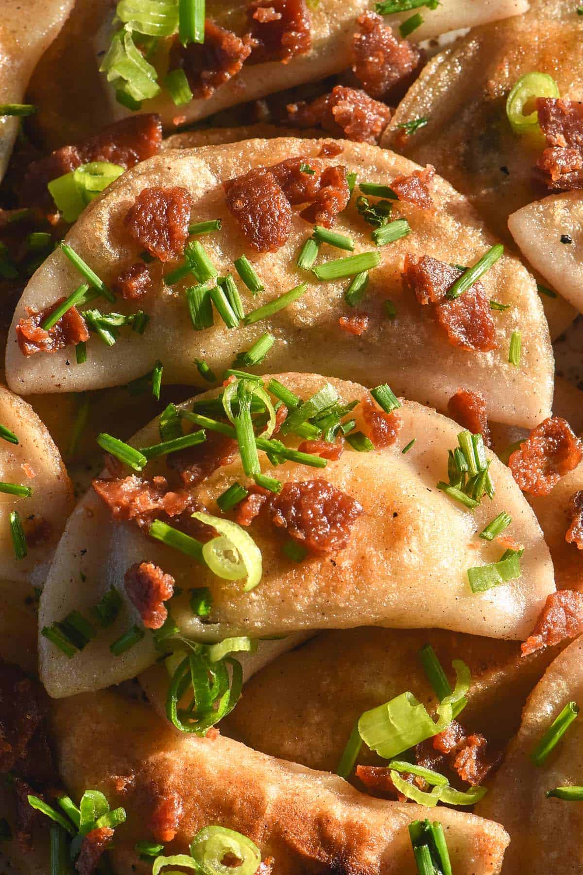 A close up image of golden fried gluten free pierogi topped with vegetarian bacon, chives