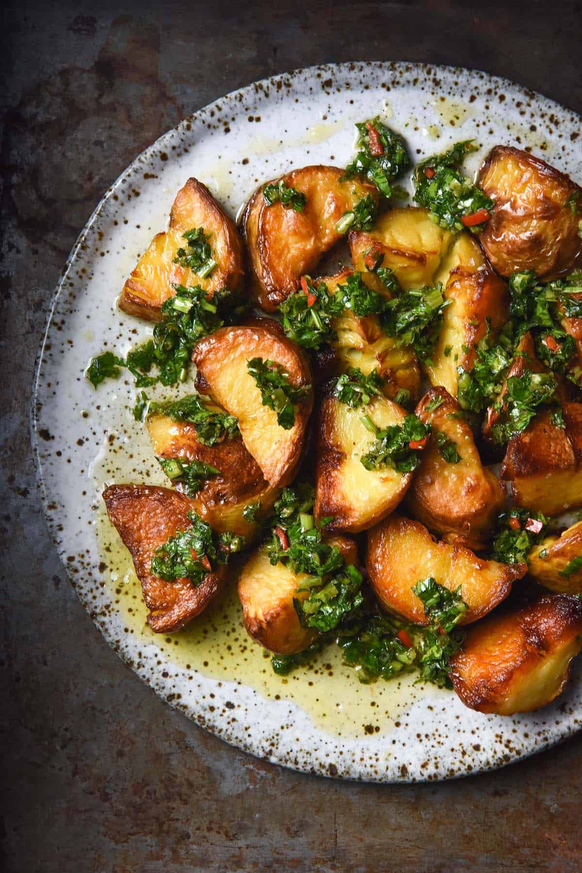 An aerial image of a white speckled ceramic plate topped with crispy potatoes and low FODMAP chimichurri. 