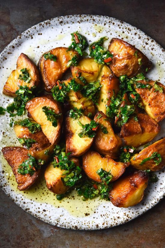 An aerial close up image of a white ceramic plate topped with crispy potatoes and low FODMAP chimichurri. The plate sits on a steel metal backdrop.
