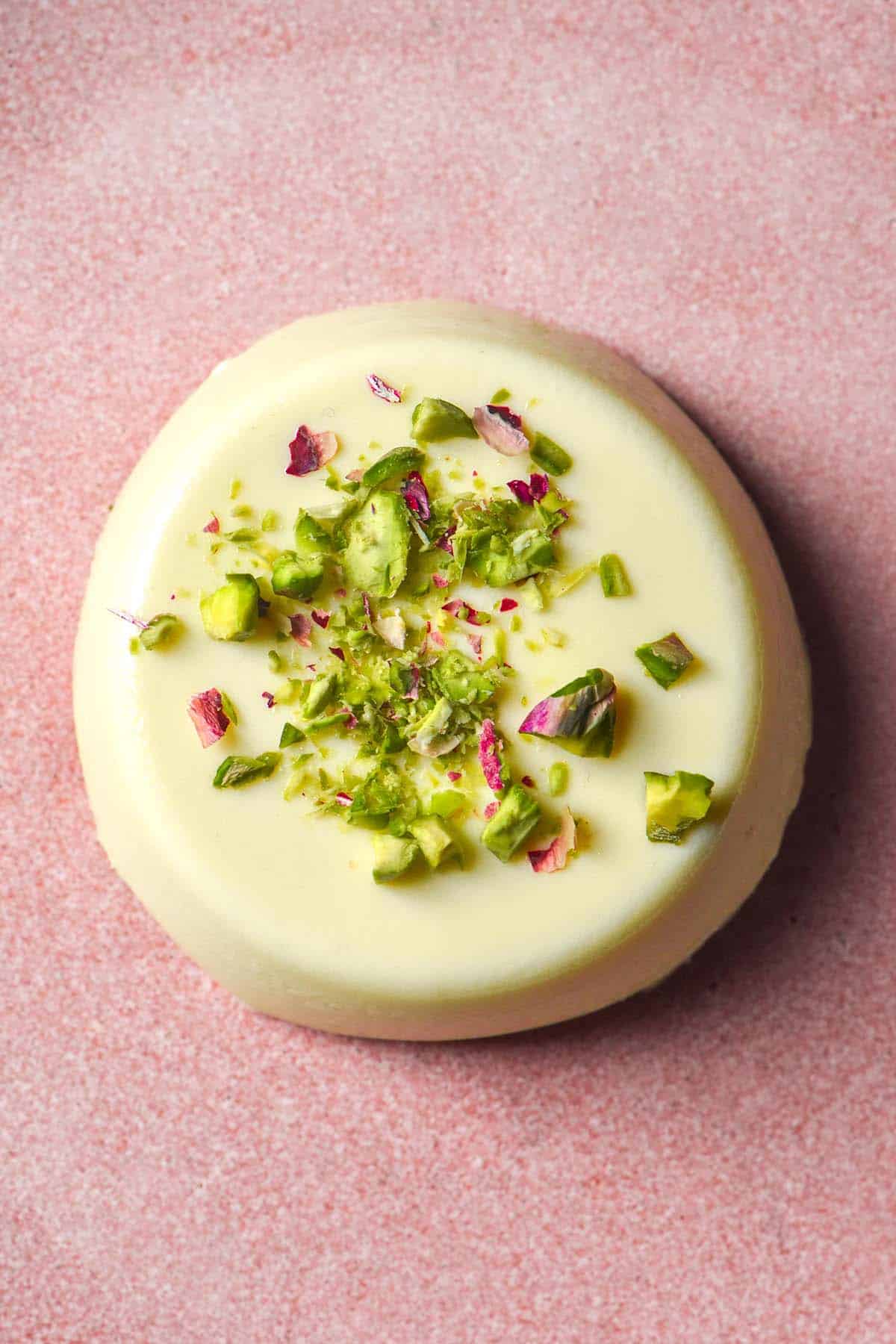 An aerial image of a panna cotta on a pale pink plate topped with finely chopped pistachios