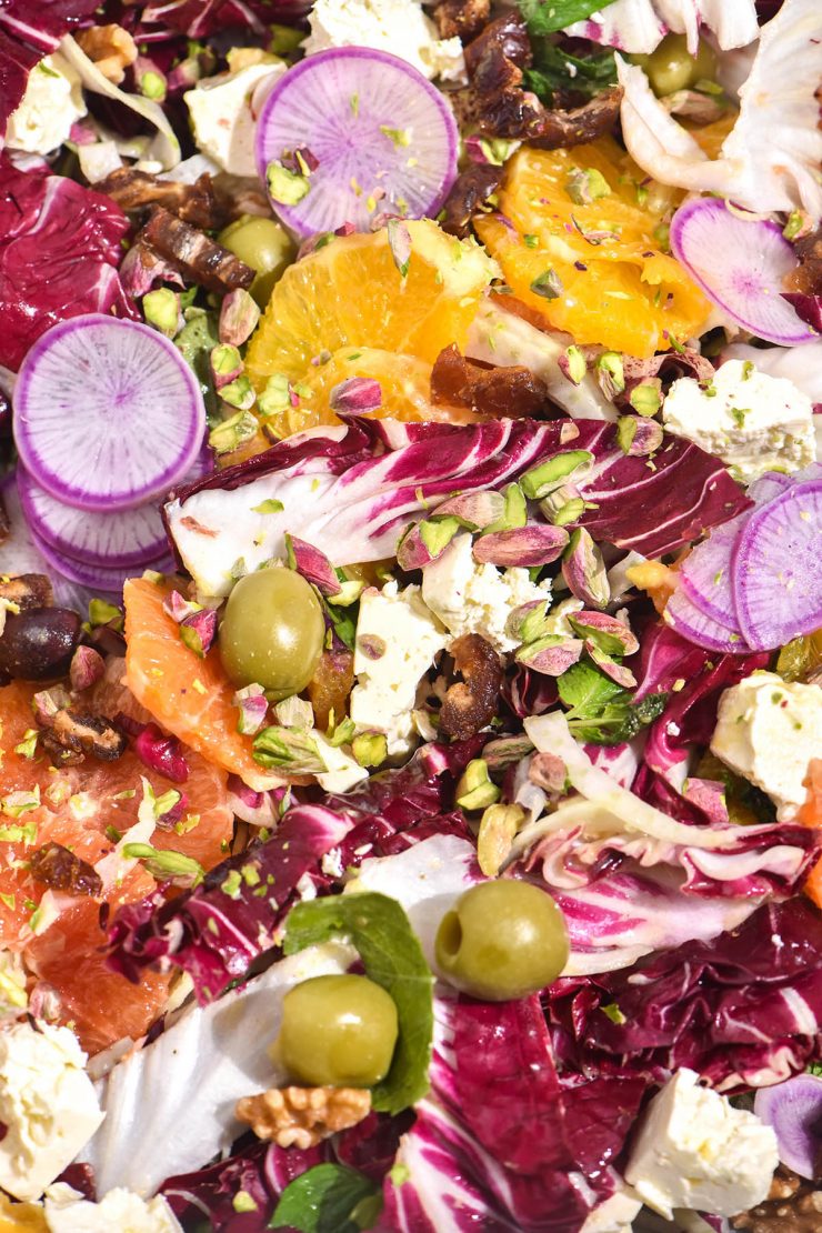 A close up macro image of a winter citrus salad in bright light. The salad contains oranges, radicchio, fennel, watermelon radishes, olives and nuts which are mixed together for a rainbow coloured salad.