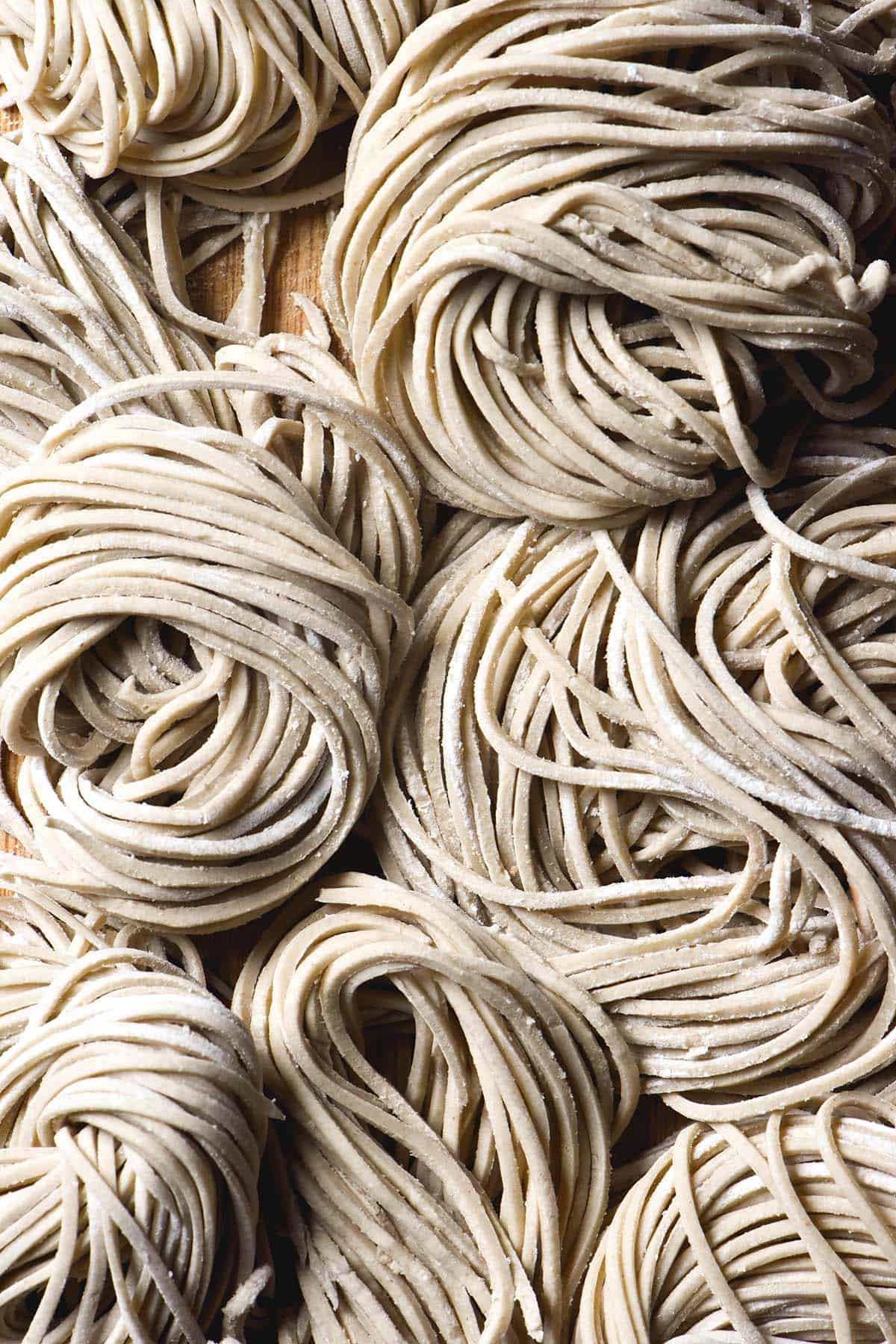 An aerial macro image of swirled raw strands of gluten free buckwheat noodles on a wooden board. 