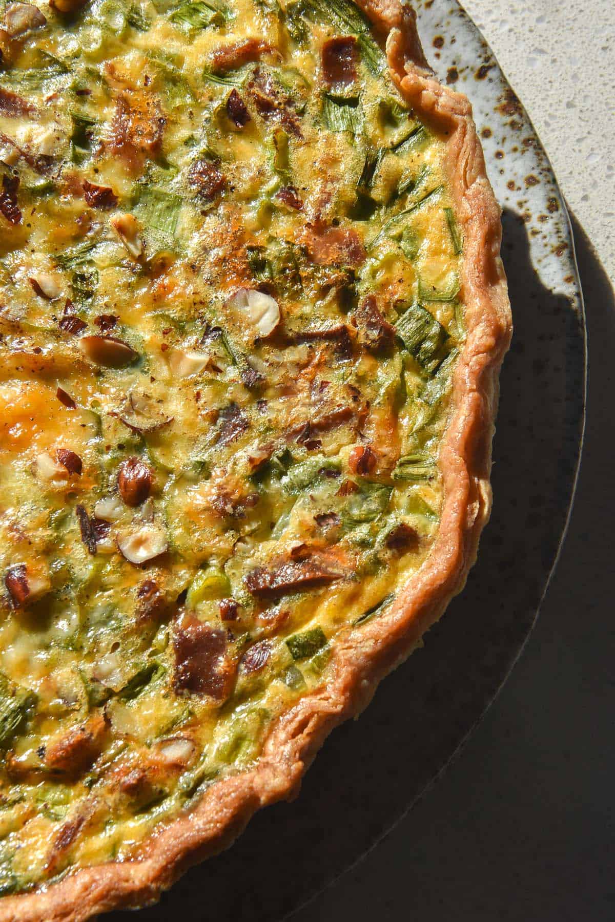 A close up aerial image of a gluten free quiche filled with spring onion greens and vegetarian bacon. 