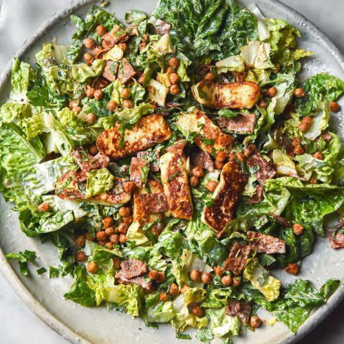 An aerial image of a haloumi salad on a large white serving platter atop a white marble table.