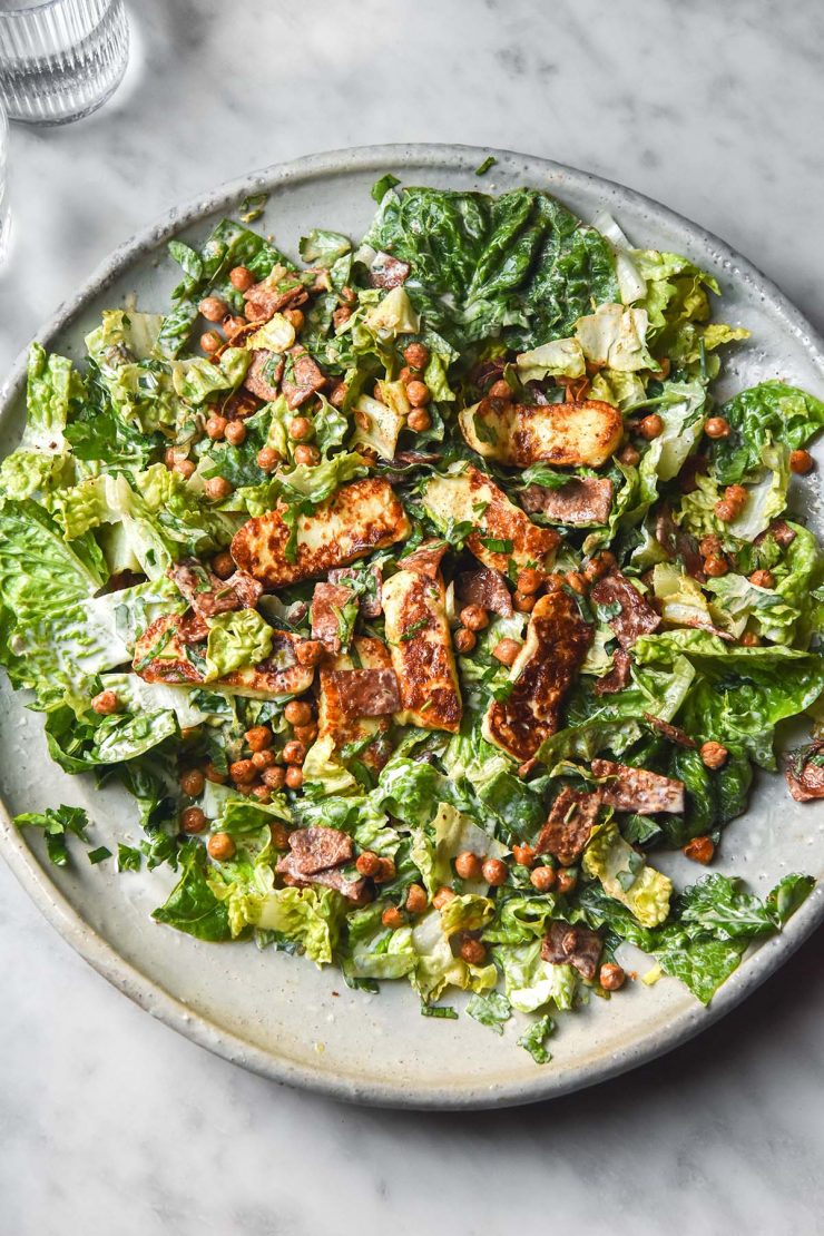 An aerial image of a haloumi salad on a large white serving platter atop a white marble table.