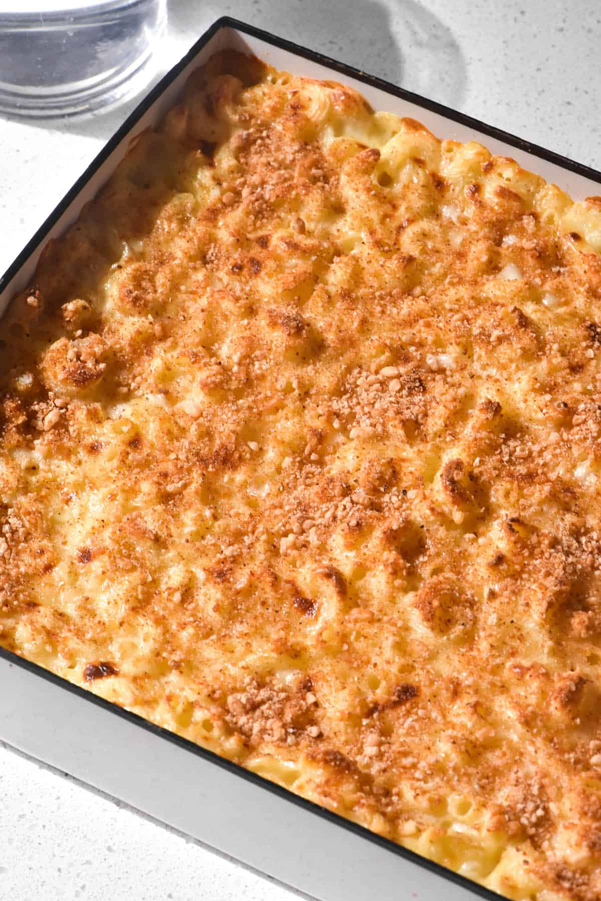 An aerial brightly lit image of a low FODMAP mac and cheese bake in a white baking dish atop a white stone benchtop.
