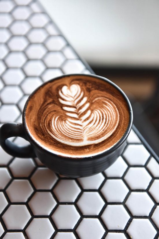 A side on image of a cappuccino with latte art atop a white hexagonal tiled table.