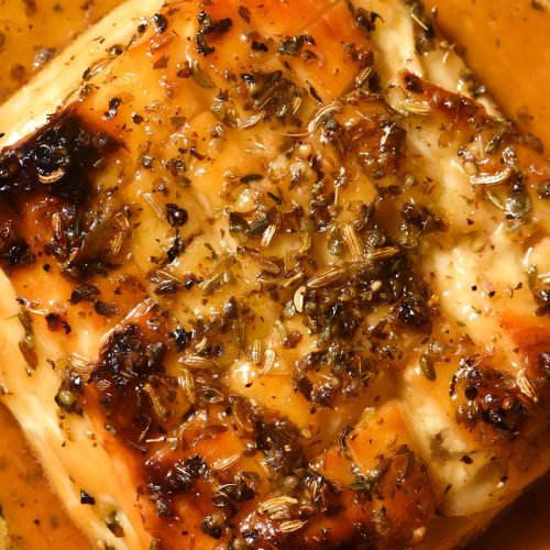 An aerial macro image of a slab of golden brown baked halloumi. The halloumi has been scored and is smothered in a maple lemon glaze. It is topped with dried oregano and fennel seeds.