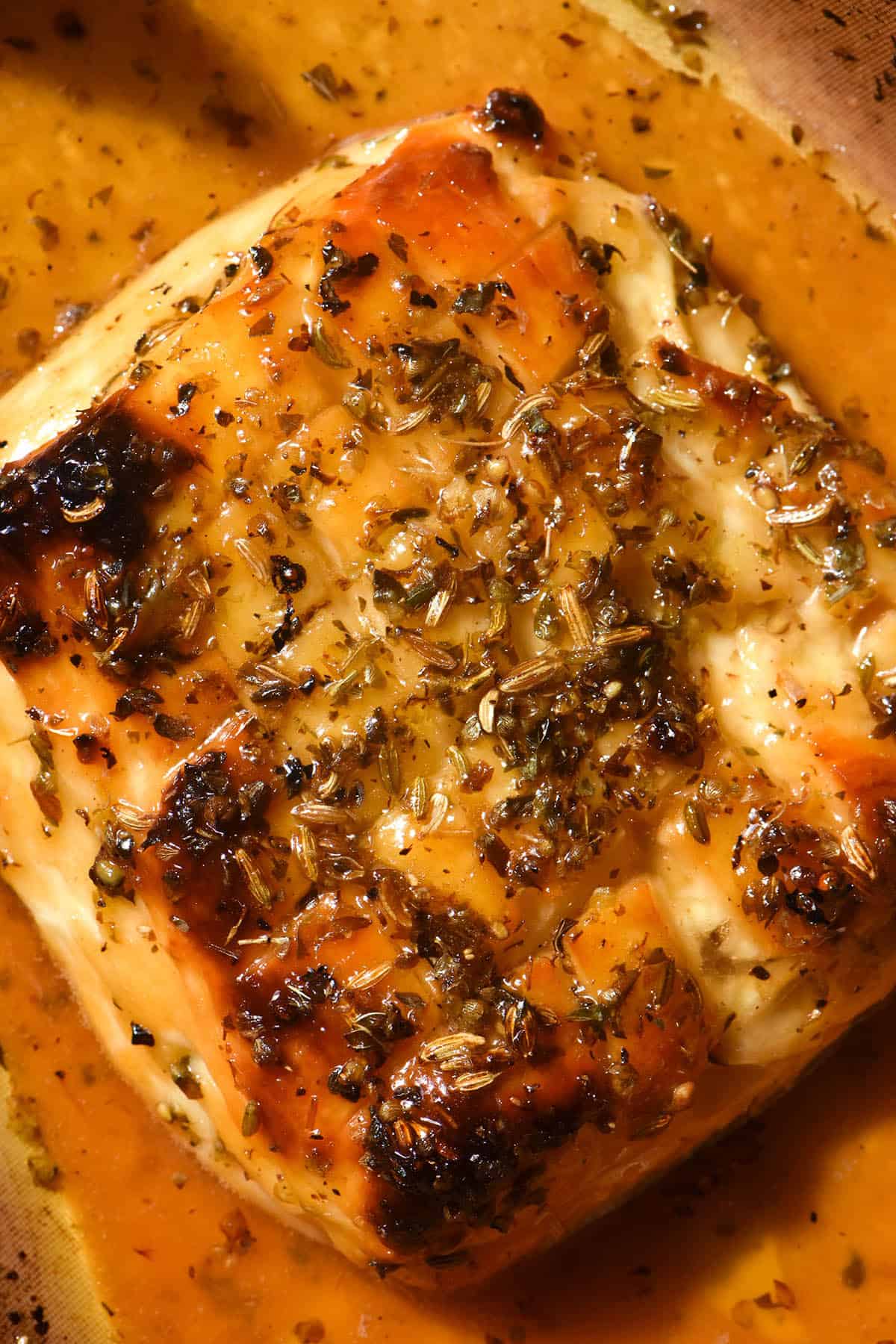 An aerial macro image of a slab of golden brown baked halloumi. The halloumi has been scored and is smothered in a maple lemon glaze. It is topped with dried oregano and fennel seeds. 