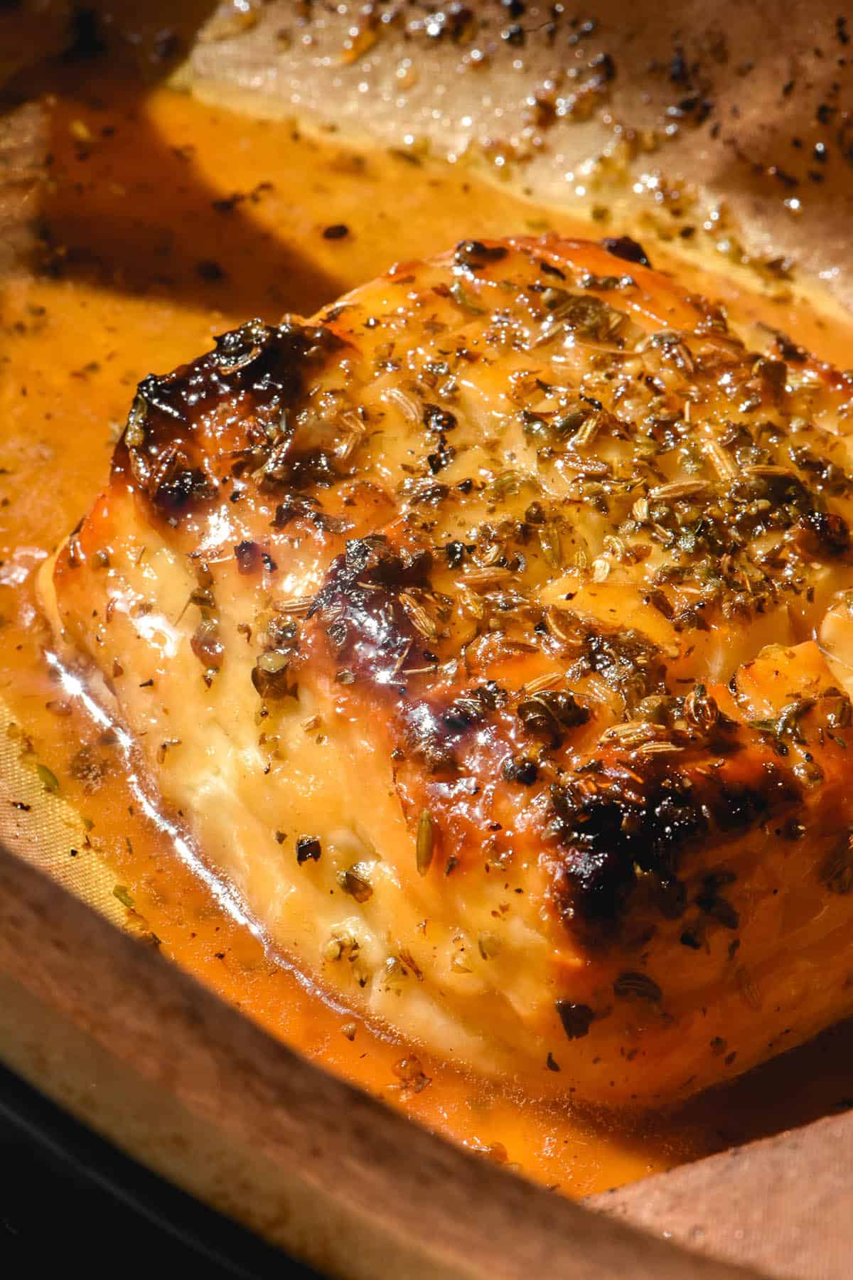 An aerial macro image of a slab of golden brown baked halloumi. The halloumi has been scored and is smothered in a maple lemon glaze. It is topped with dried oregano and fennel seeds. 