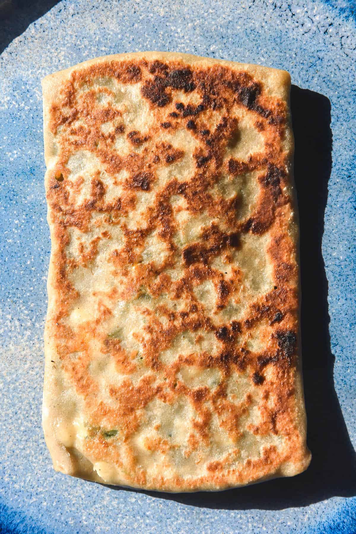 An aerial macro image of a deeply golden gluten free gozleme atop a bright blue ceramic plate
