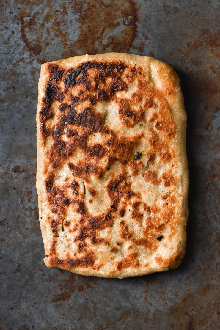 An aerial image of a deeply golden gluten free gozleme atop a dark steel metal backdrop