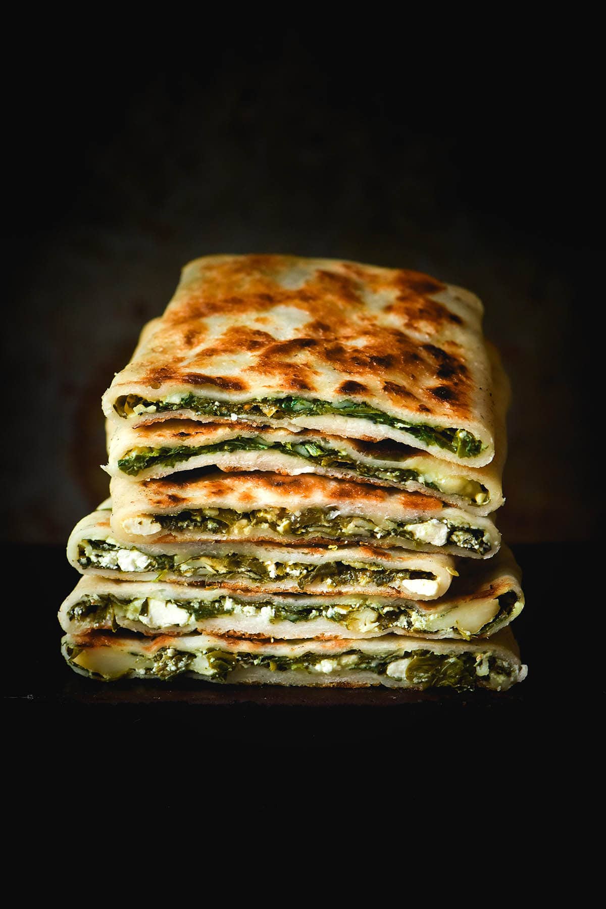 A dark and moody side on image of a stack of gluten free gozleme stuffed with spinach and feta.