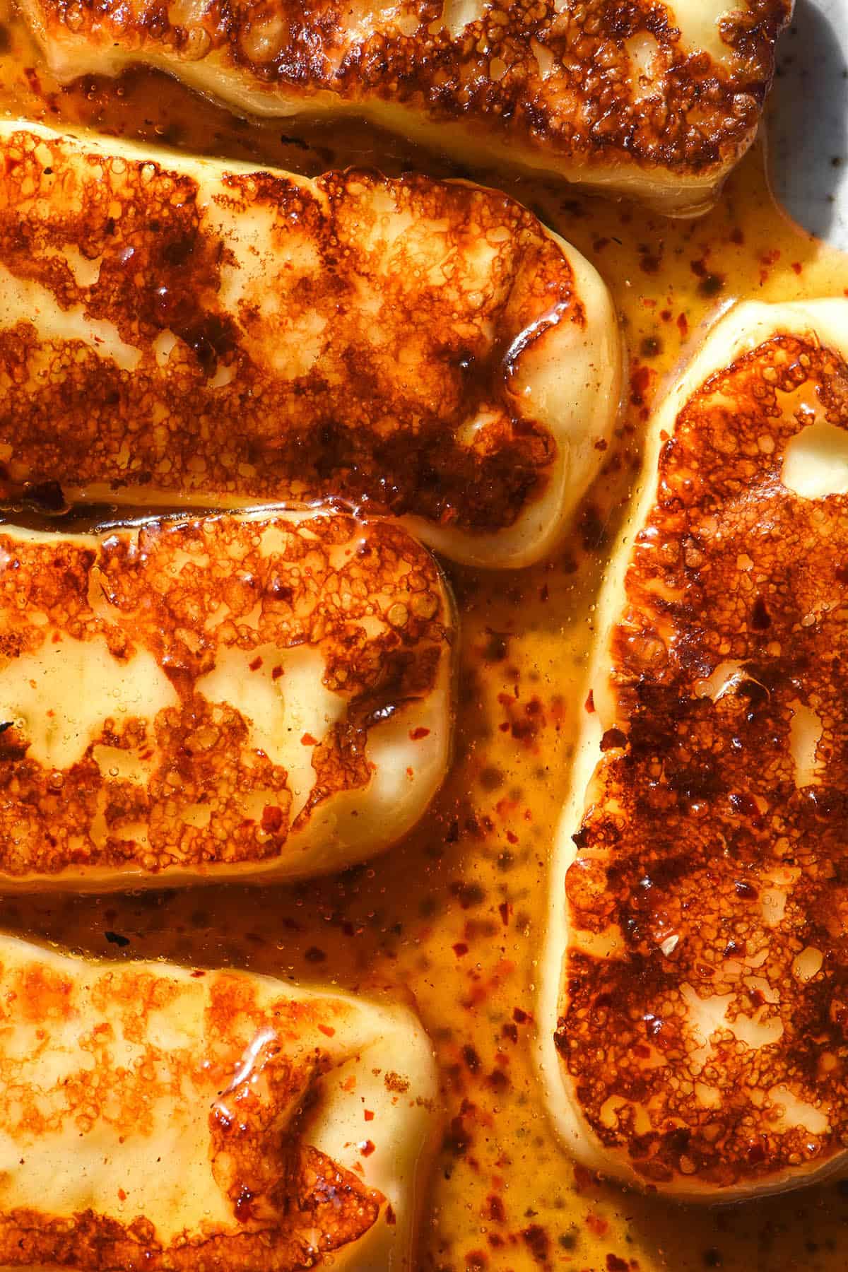 An aerial image of golden brown honey halloumi on a white speckled ceramic plate. The halloumi is smothered in a honey, lemon and chilli sauce.