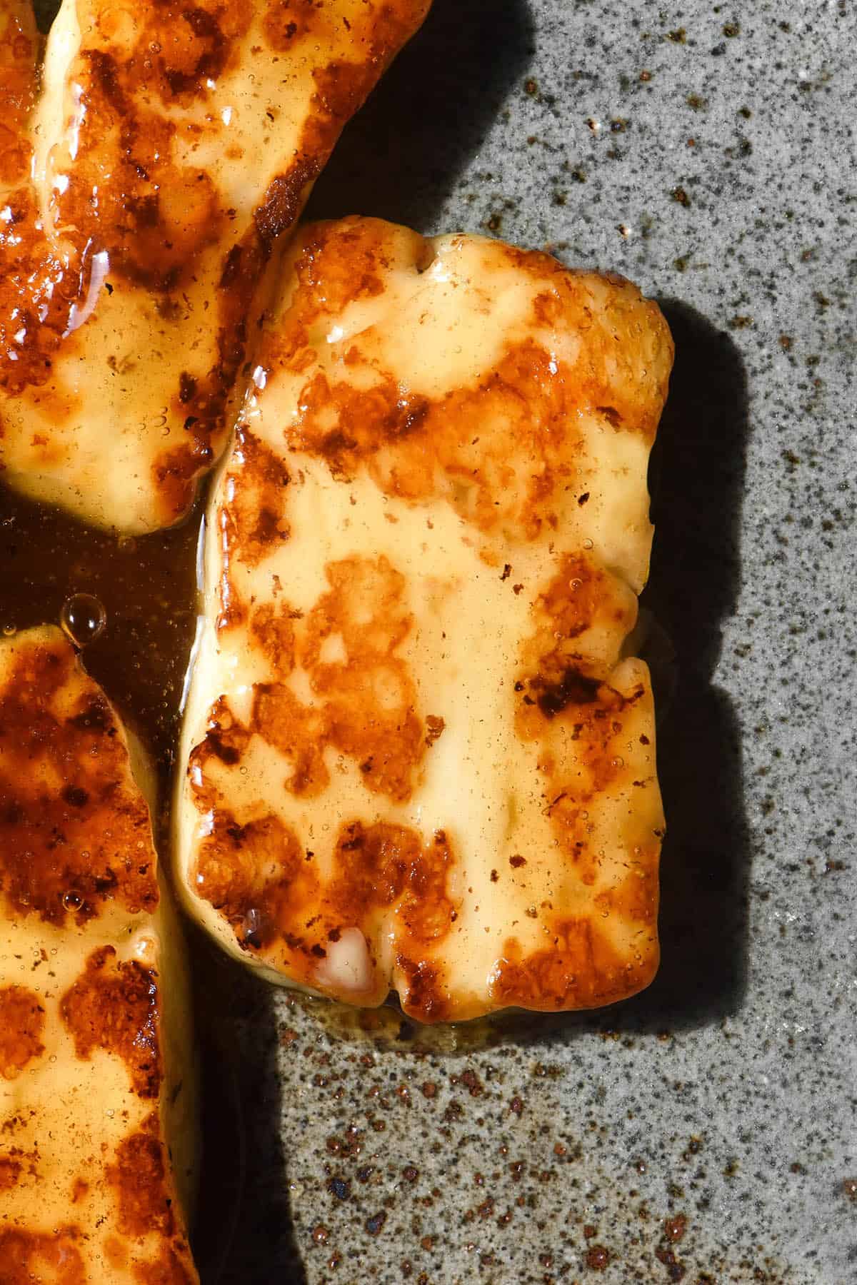 An aerial image of golden brown honey glazed halloumi on a dark blue speckled ceramic plate