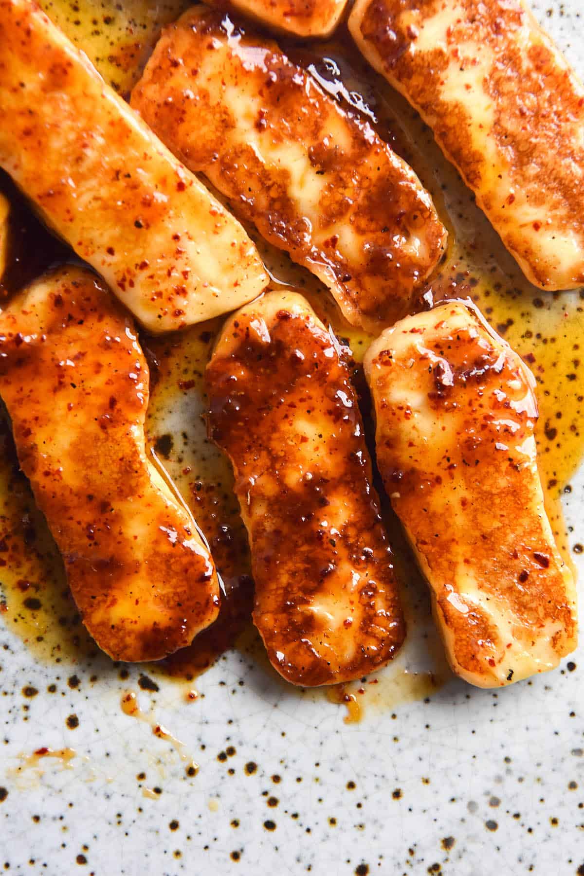An aerial close up image of honey glazed halloumi slices on a white speckled ceramic plate