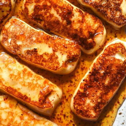 An aerial close up image of honey glazed halloumi slices on a white speckled ceramic plate