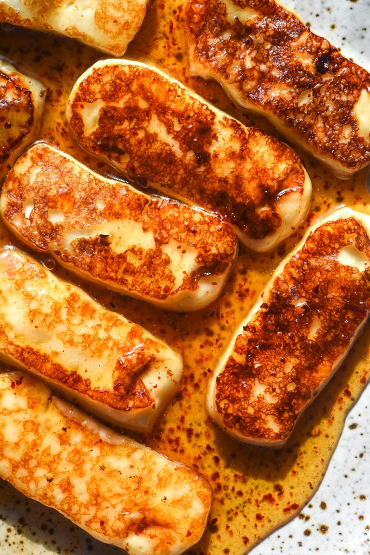 An aerial close up image of honey glazed halloumi slices on a white speckled ceramic plate