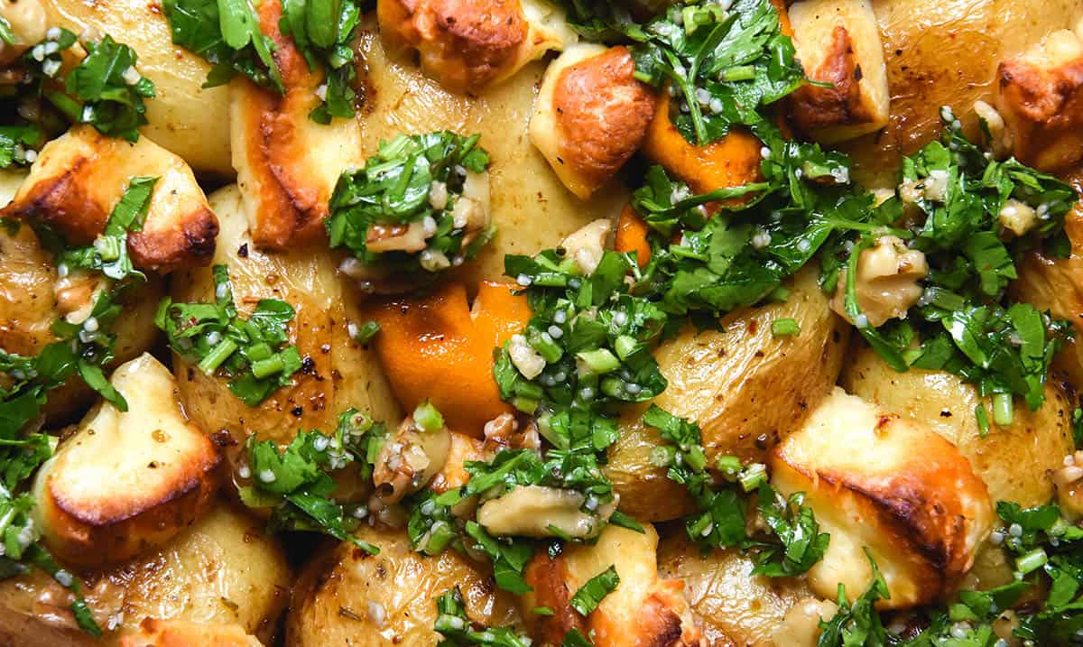 A close up macro image of lemon roasted potatoes with golden brown haloumi and a herb walnut salsa