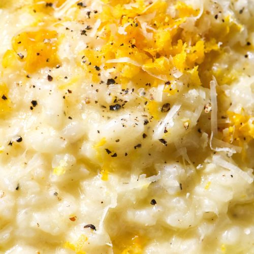 An aerial close up image of a plate of low FODMAP risotto al limone topped with lemon zest, parmesan and garlic infused oil