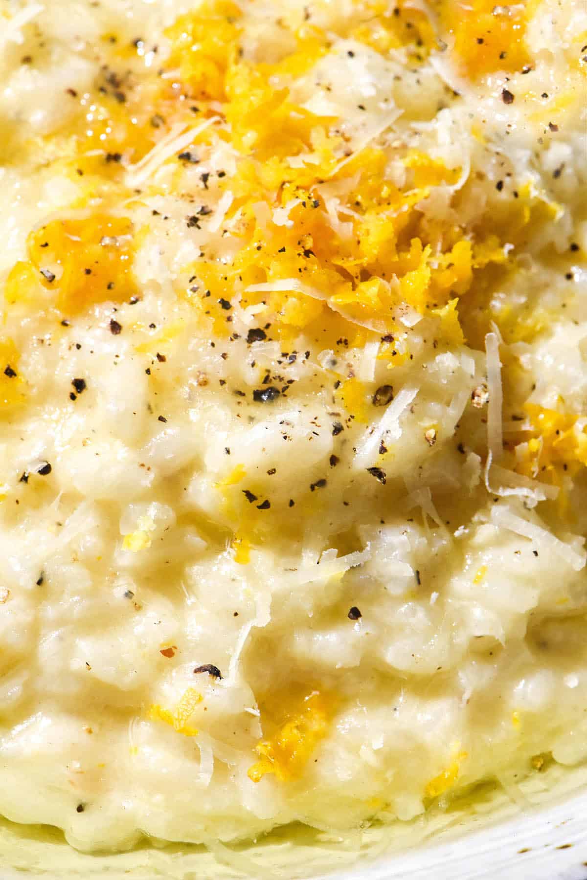 A close up macro image of a bowl of risotto al limone topped with grated parmesan, garlic infused oil, lemon zest and cracked black pepper. 