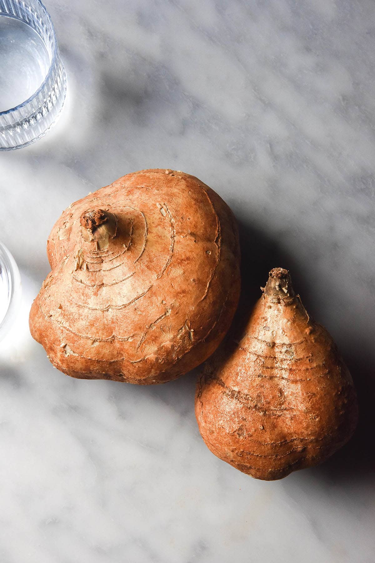 An aerial image of two jicama on a white marble table. Two glasses of water sit to the top left of the image.