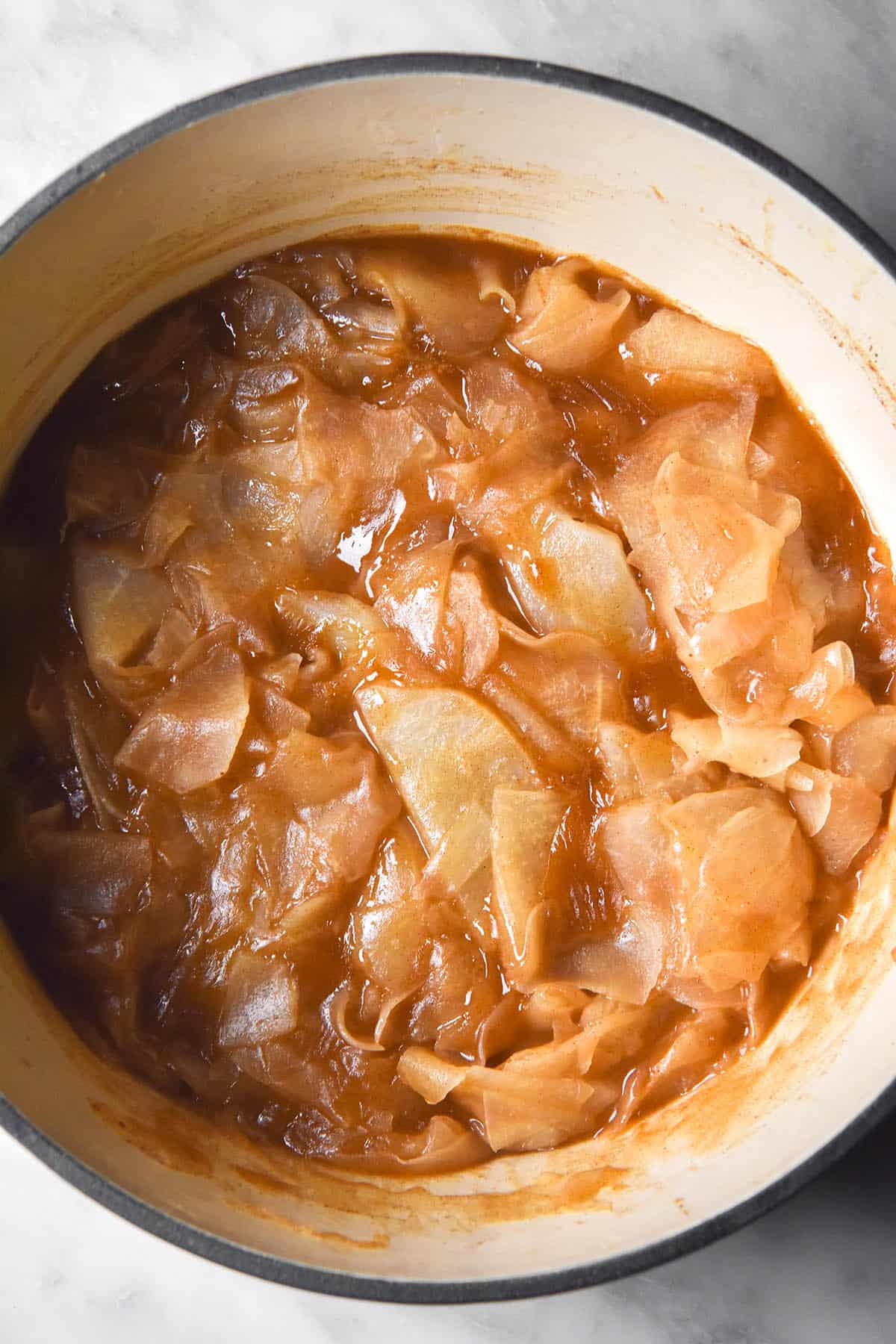 An aerial image of a large pot filled with low FODMAP stewed apple. The pot has a beige interior, olive green exterior and sits on a white marble table.