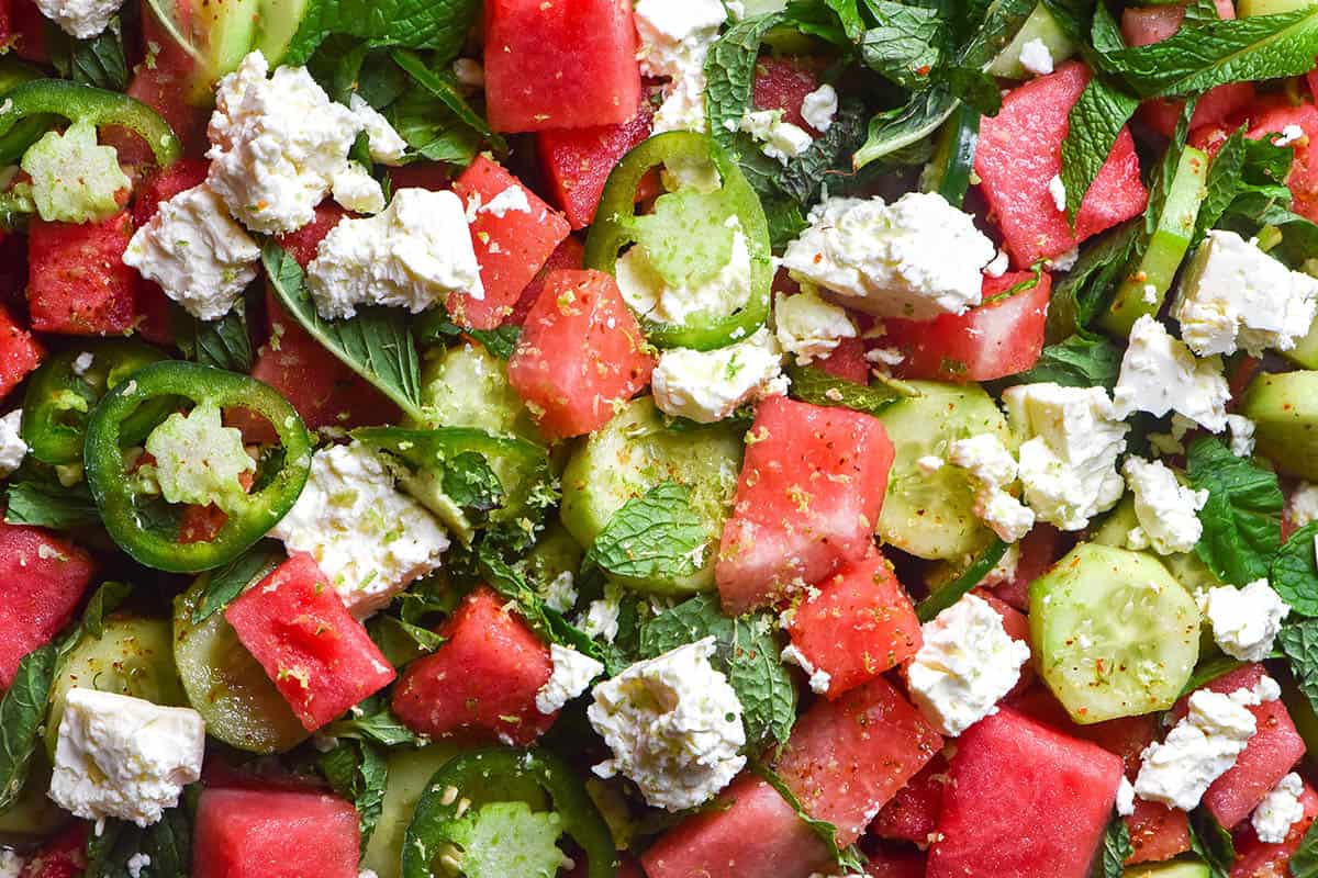 An aerial macro image of a watermelon and tajin salad with feta, cucumber, jalapeno slices, mint and lime zest