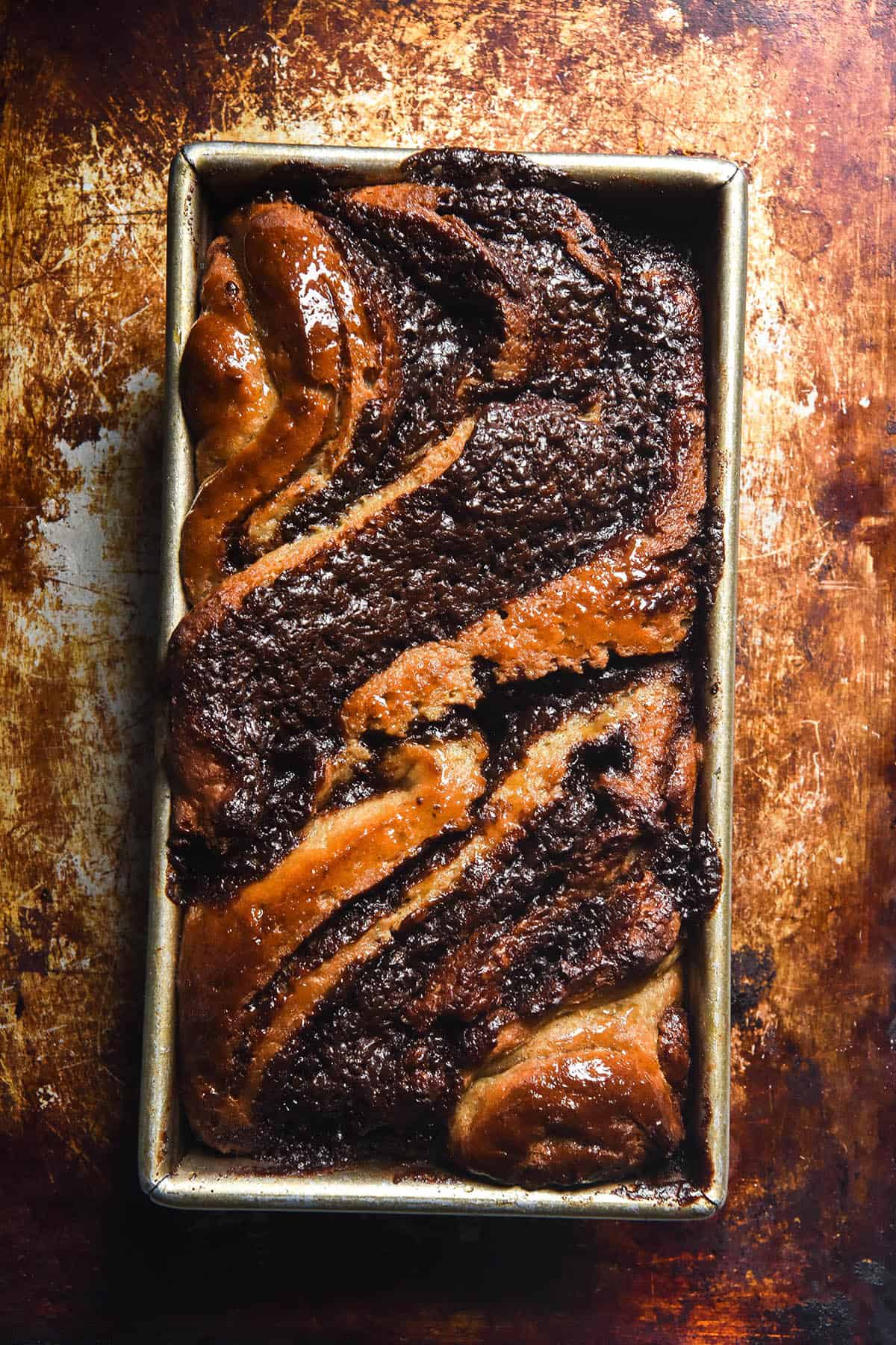 An aerial image of a buckwheat babka with chocolate swirls on a mottled brown baking tray.