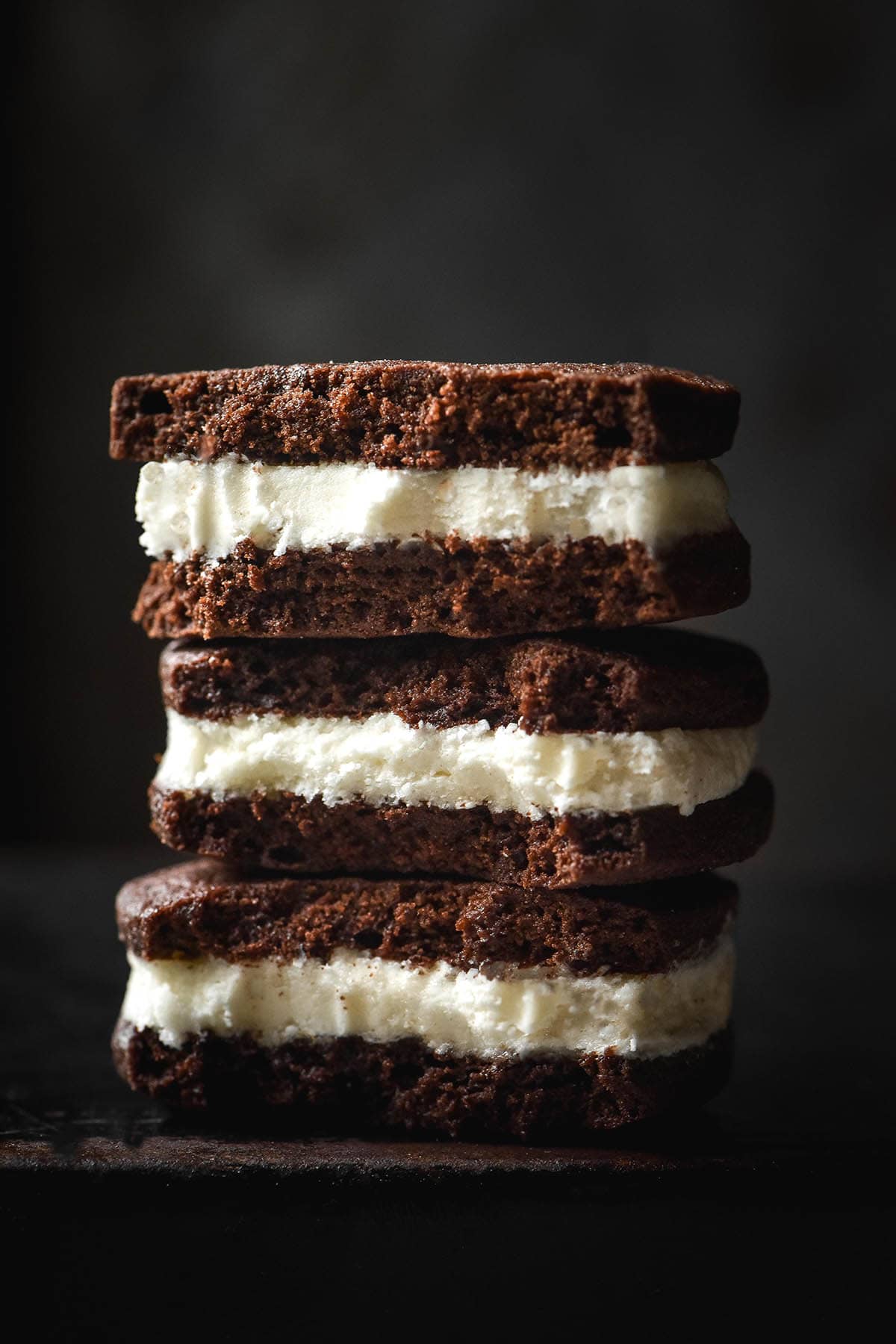 A macro side on image of a stack of gluten free chocolate sandwich cookies that have been bitten, revealing the white buttercream inside. 