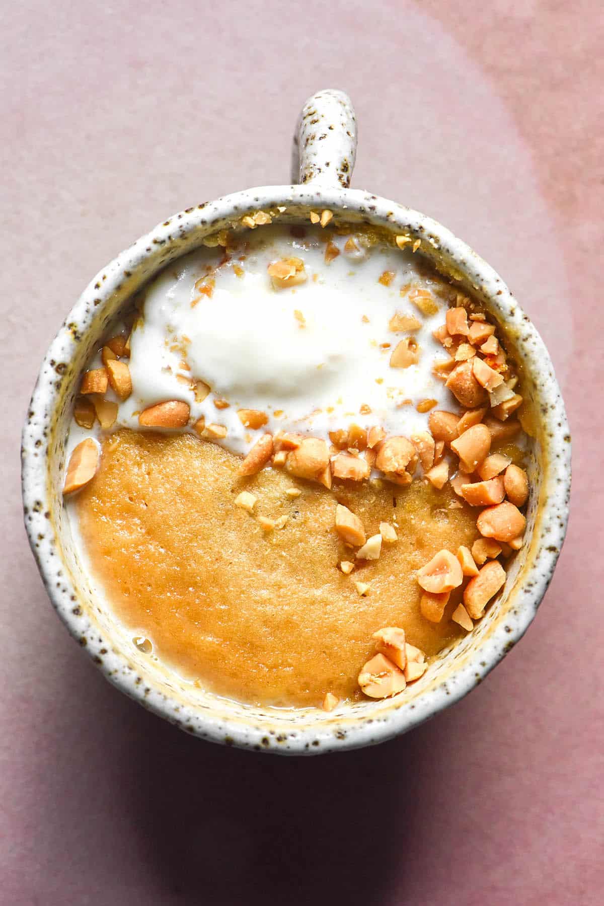 An aerial image of a gluten free peanut butter mug cake topped with chopped peanuts and vanilla ice cream on a pale pink ceramic plate