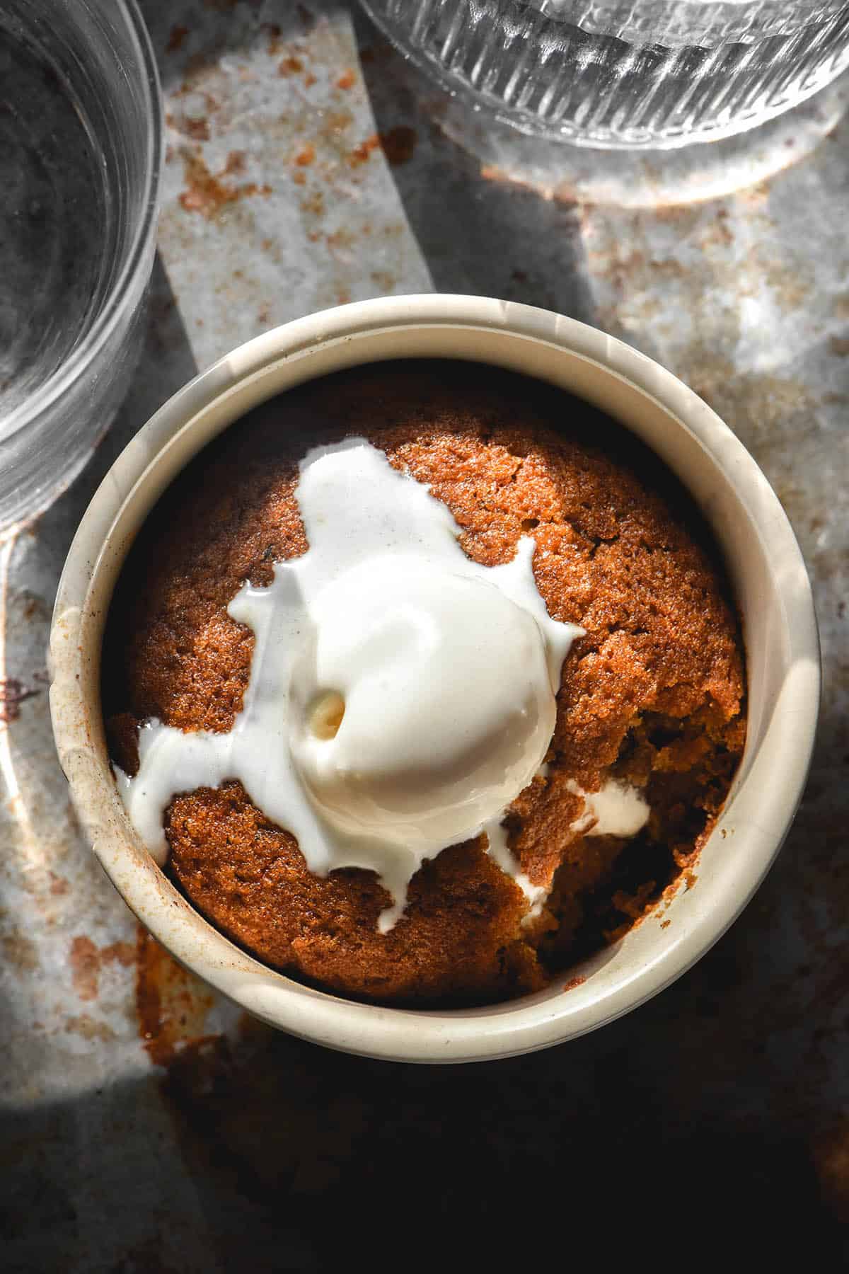 An aerial image of a gluten free sticky date pudding mug cake in a ramekin on a steel backdrop