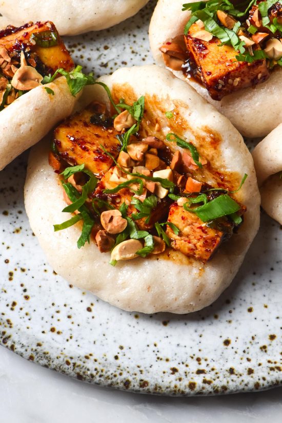 An aerial image of gluten free bao buns stuffed with chilli tofu on a white speckled ceramic plate