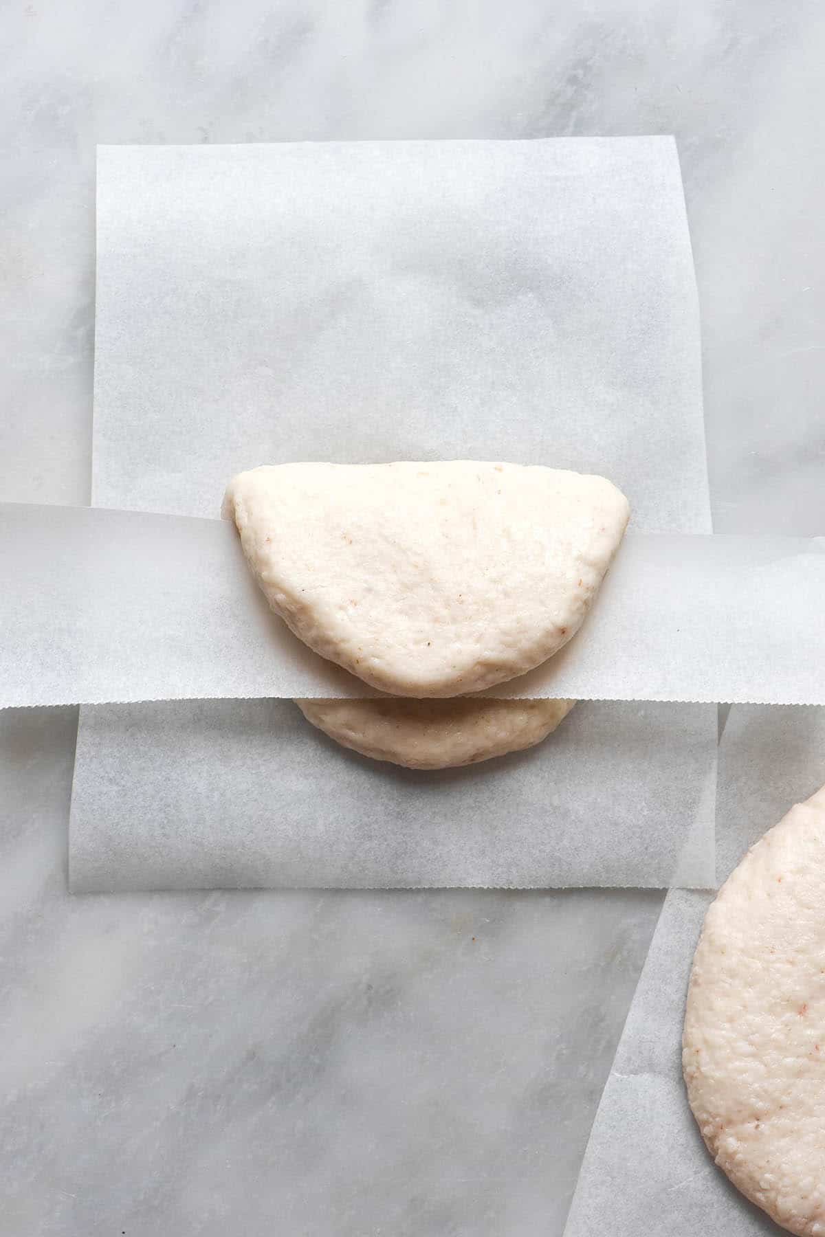 An instructional image regarding how to shape gluten free bao buns. The unshaped buns sit on a white marble table