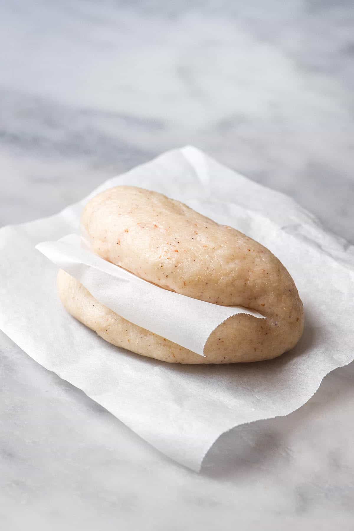 An image of a gluten free bao bun on a piece of baking paper atop a white marble table 
