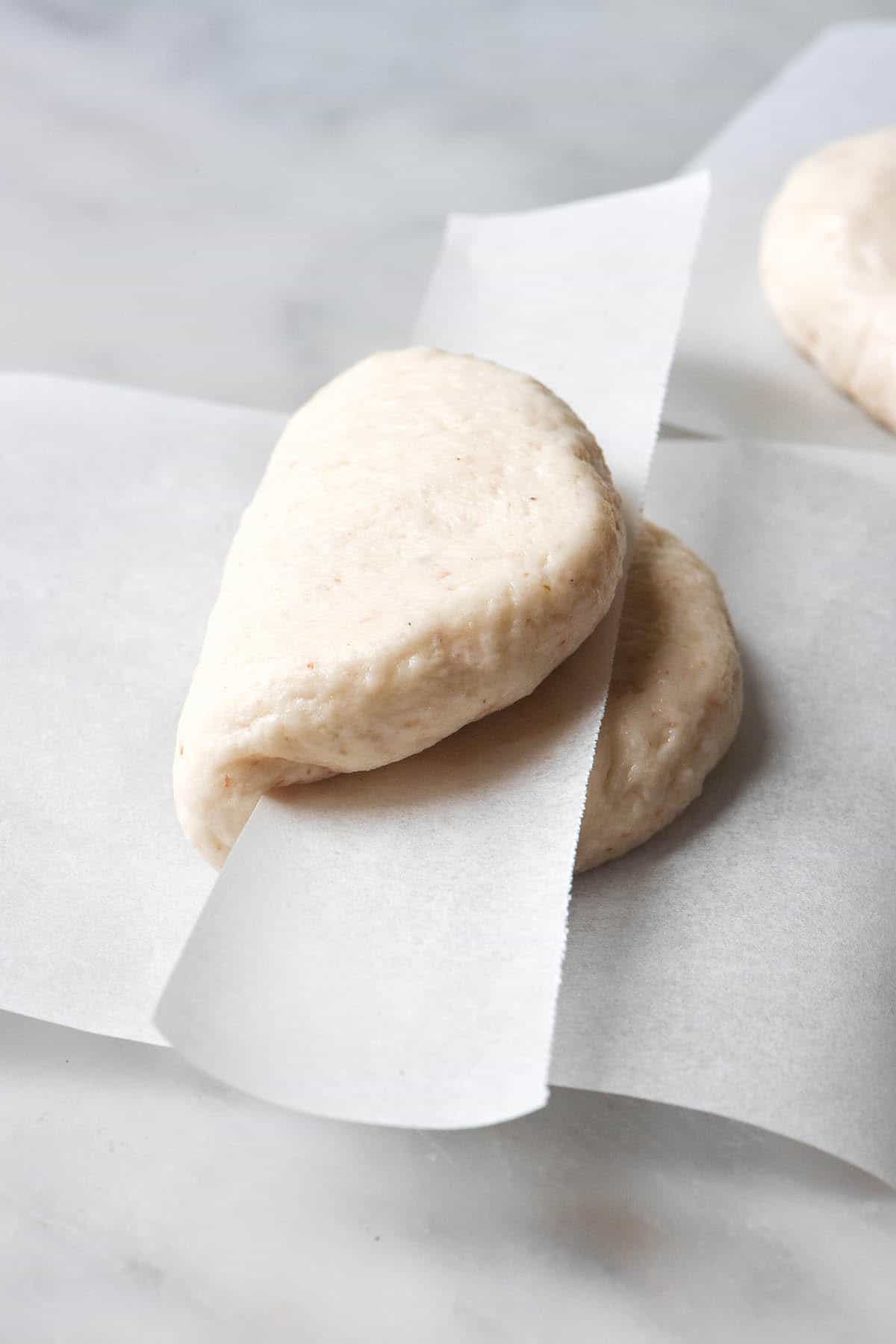 An instructional image regarding how to shape gluten free bao buns. The unshaped buns sit on a white marble table