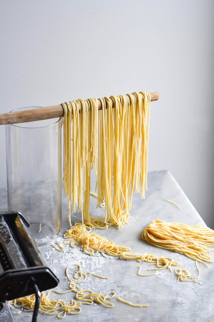 A side on image of gluten free egg noodles draped over a wooden spoon against a white backdrop