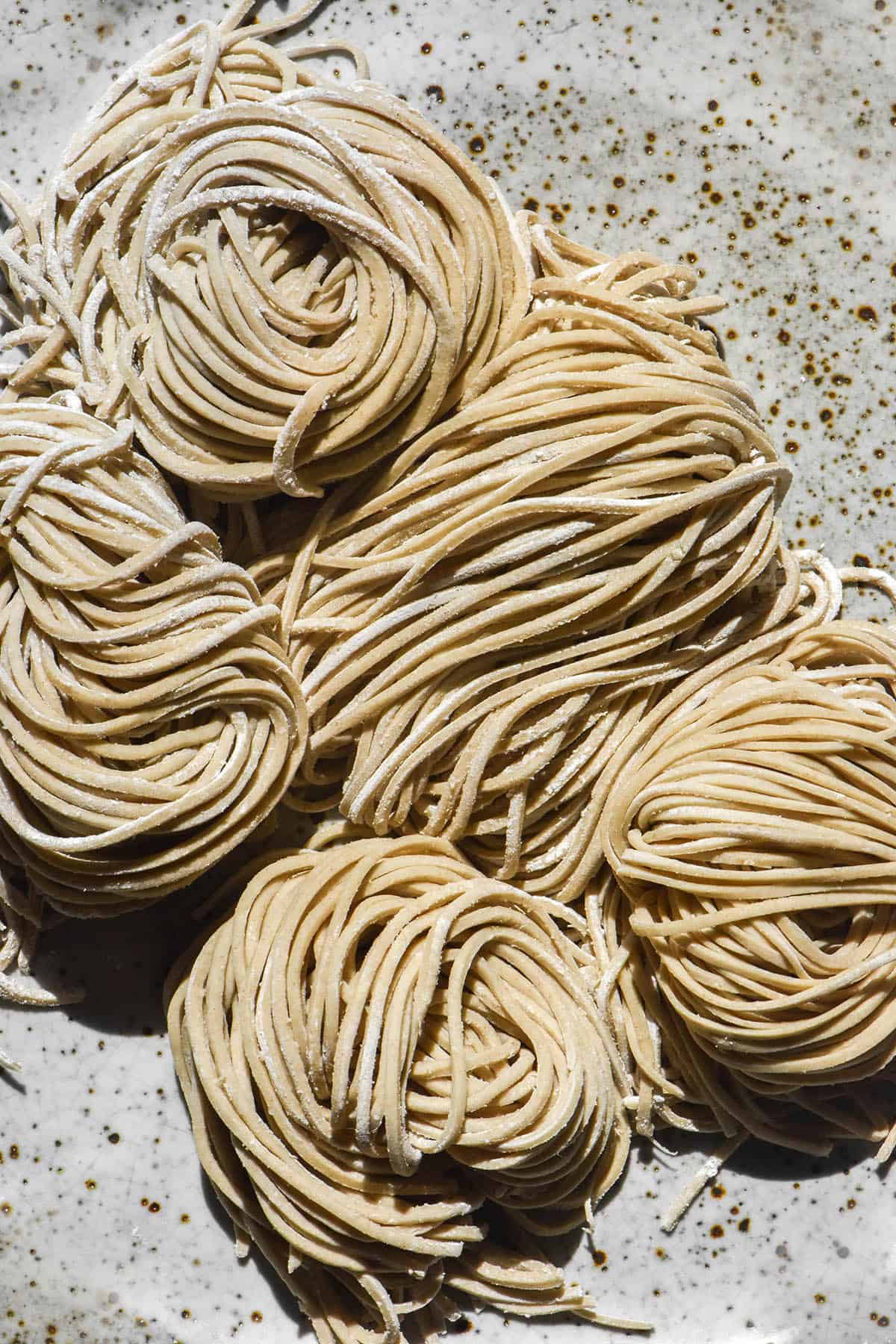 An aerial close up image of gluten free buckwheat soba noodles arranged in nests on a white speckled ceramic plate