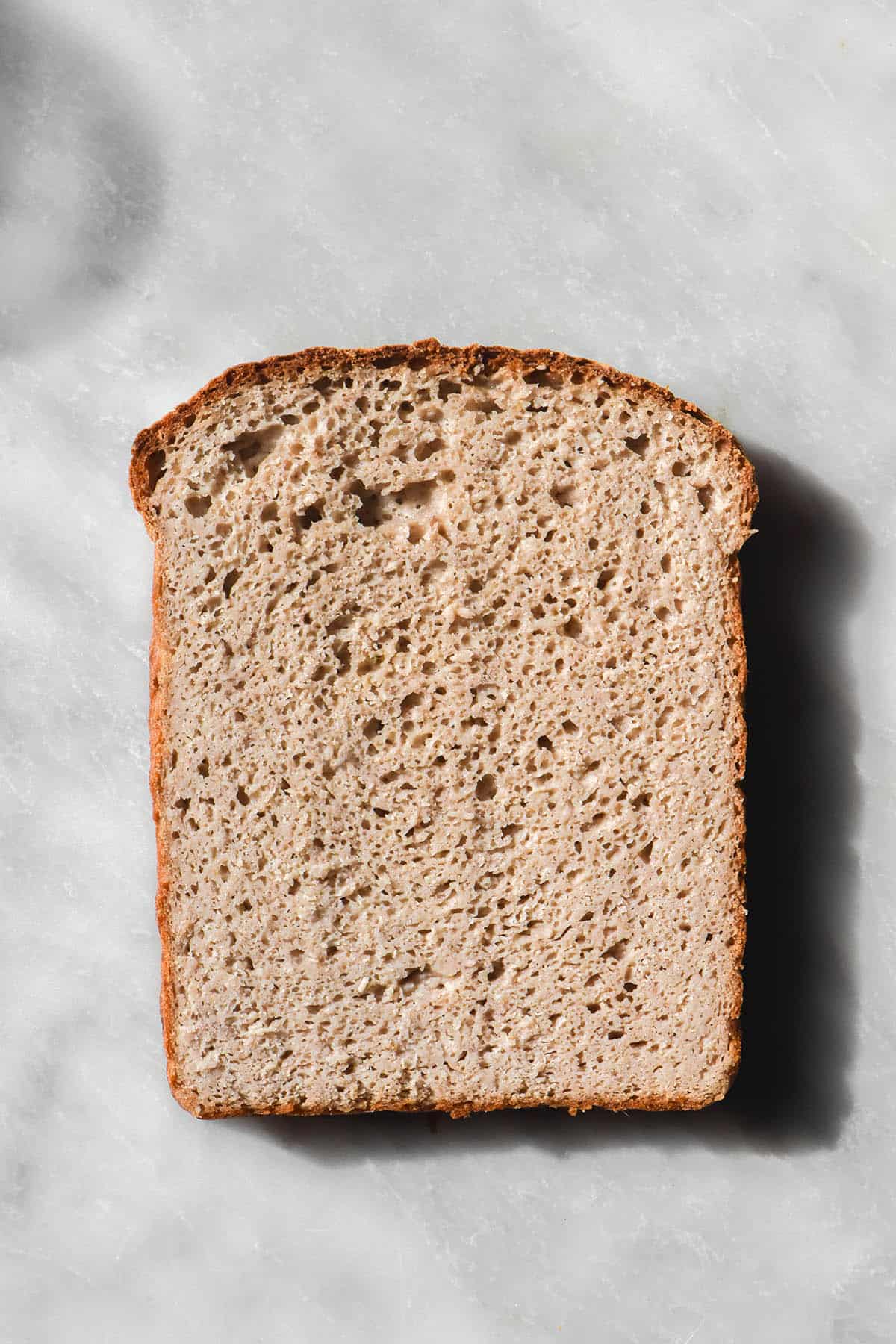 An aerial close up image of the crumb of a slice of gluten free vegan high protein bread atop a white marble table